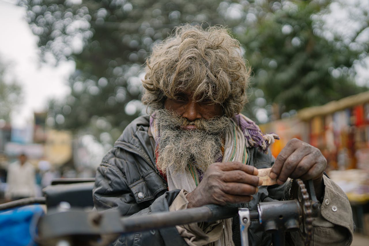 An elderly man with a rugged appearance focuses on repair work in the bustling streets of Varanasi, India.