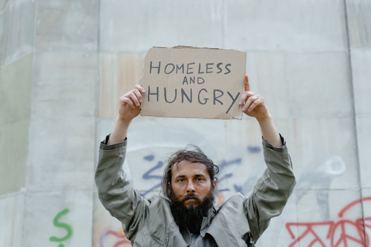 A homeless man holds a cardboard sign reading 'Homeless and Hungry.'